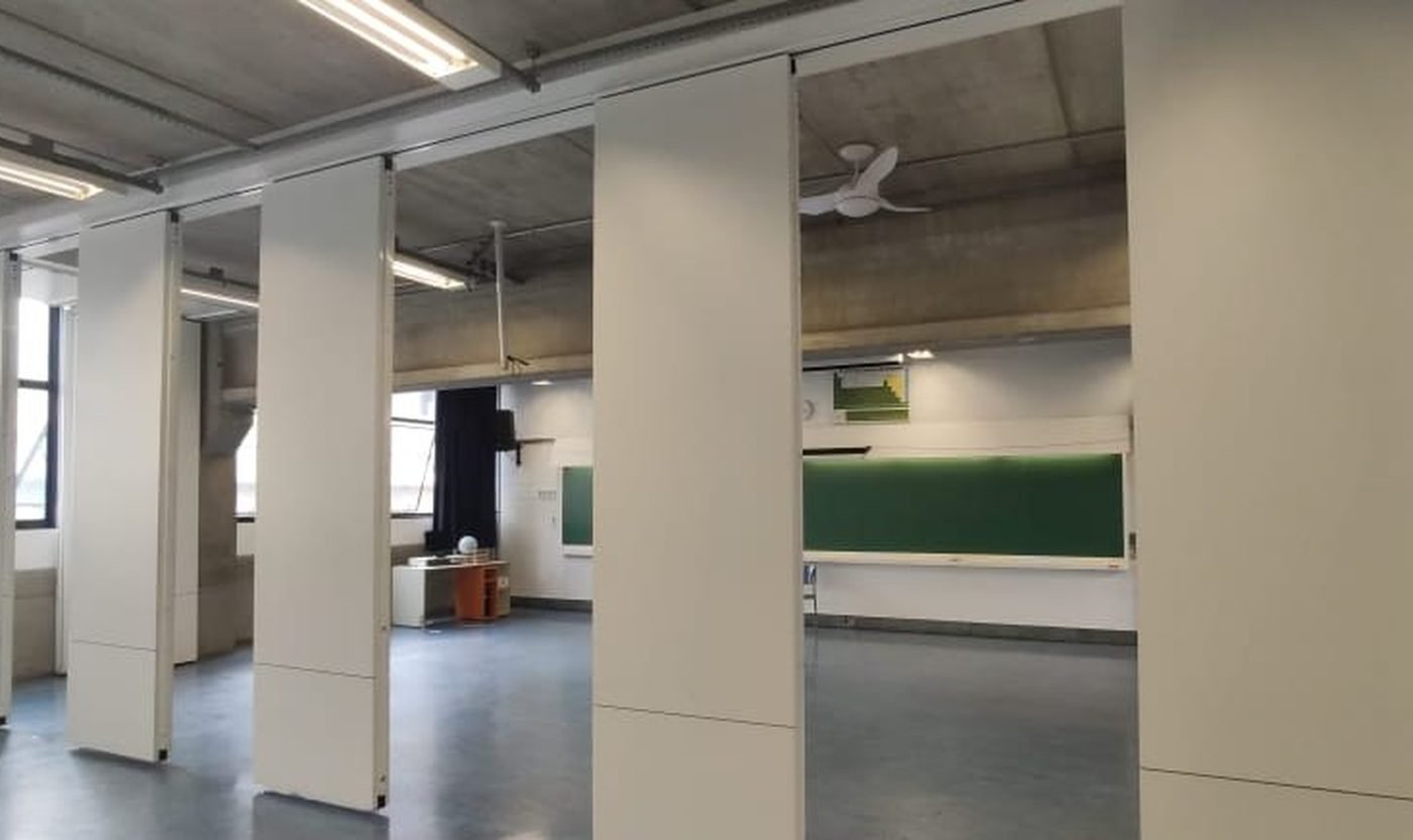 Sala de aula dividida por painéis removíveis, em deslocamento pela guia do teto.