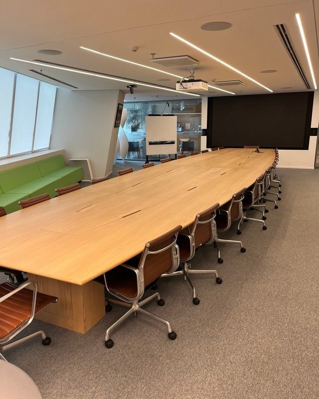 Sala de reunião com mesa longa de madeira e cadeiras de couro.