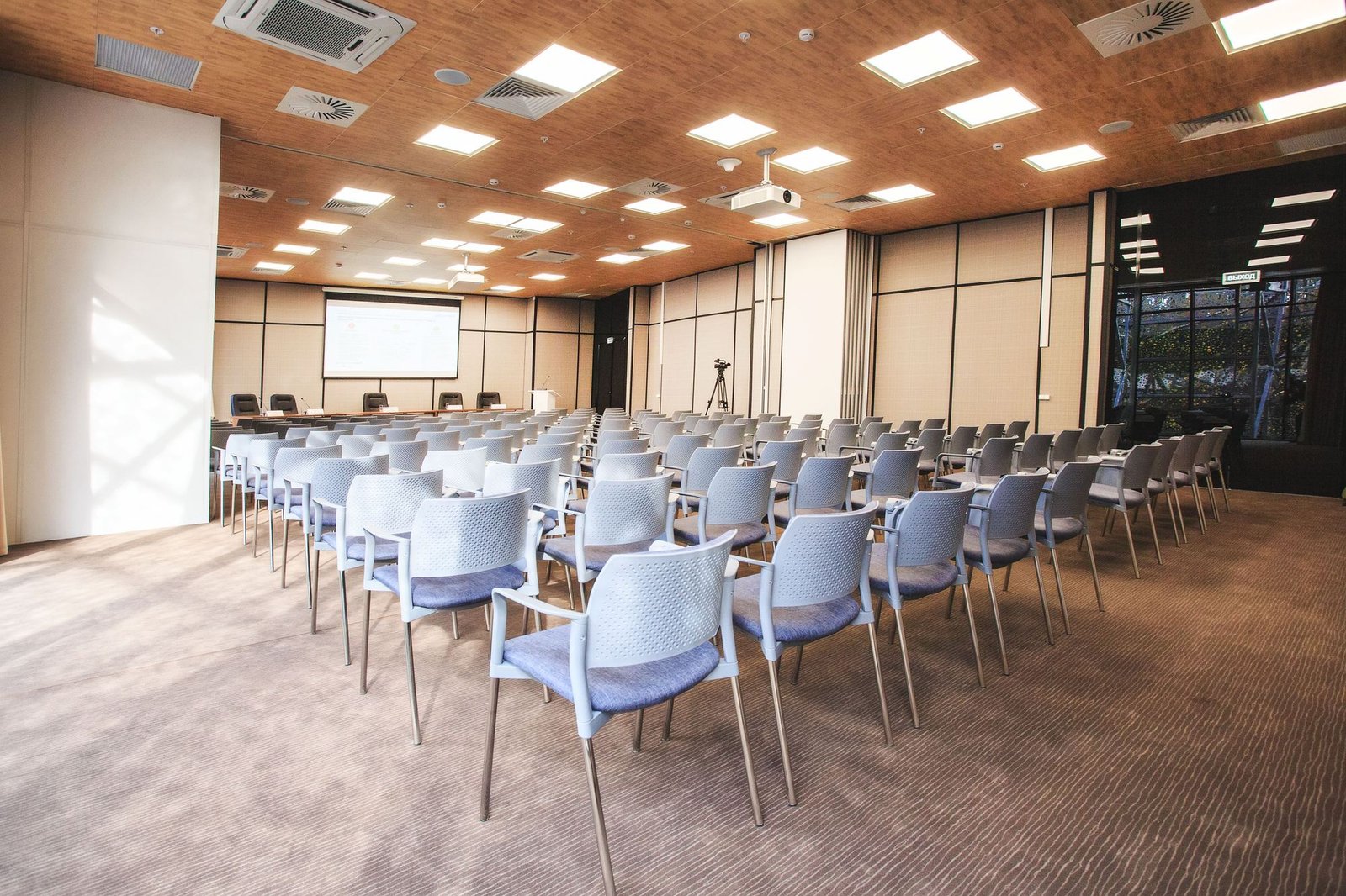 Auditório corporativo montado, com fileiras de cadeiras, tela de projeção e forro de madeira.